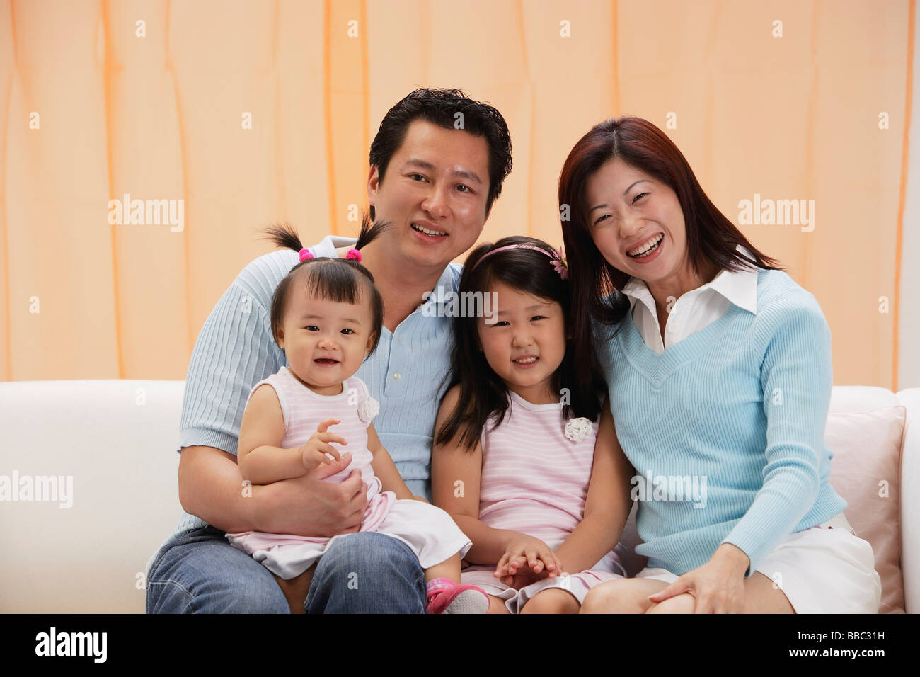Porträt der Familie von 4, Mama, Papa und zwei Töchter, auf Couch sitzen, Lächeln, Blick in die Kamera Stockfoto