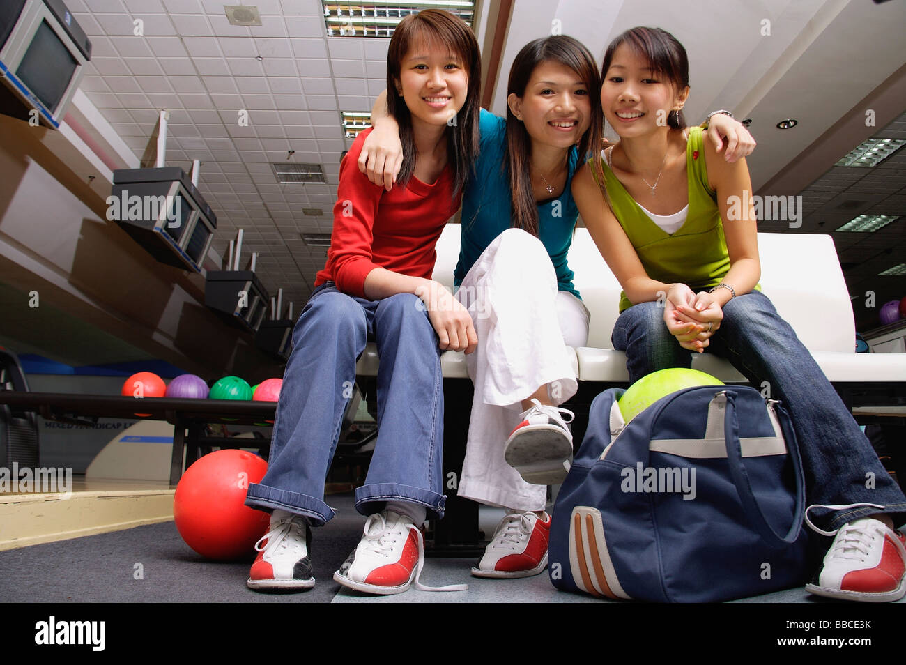Frauen sitzen nebeneinander in eine Bowlingbahn in die Kamera Lächeln Stockfoto