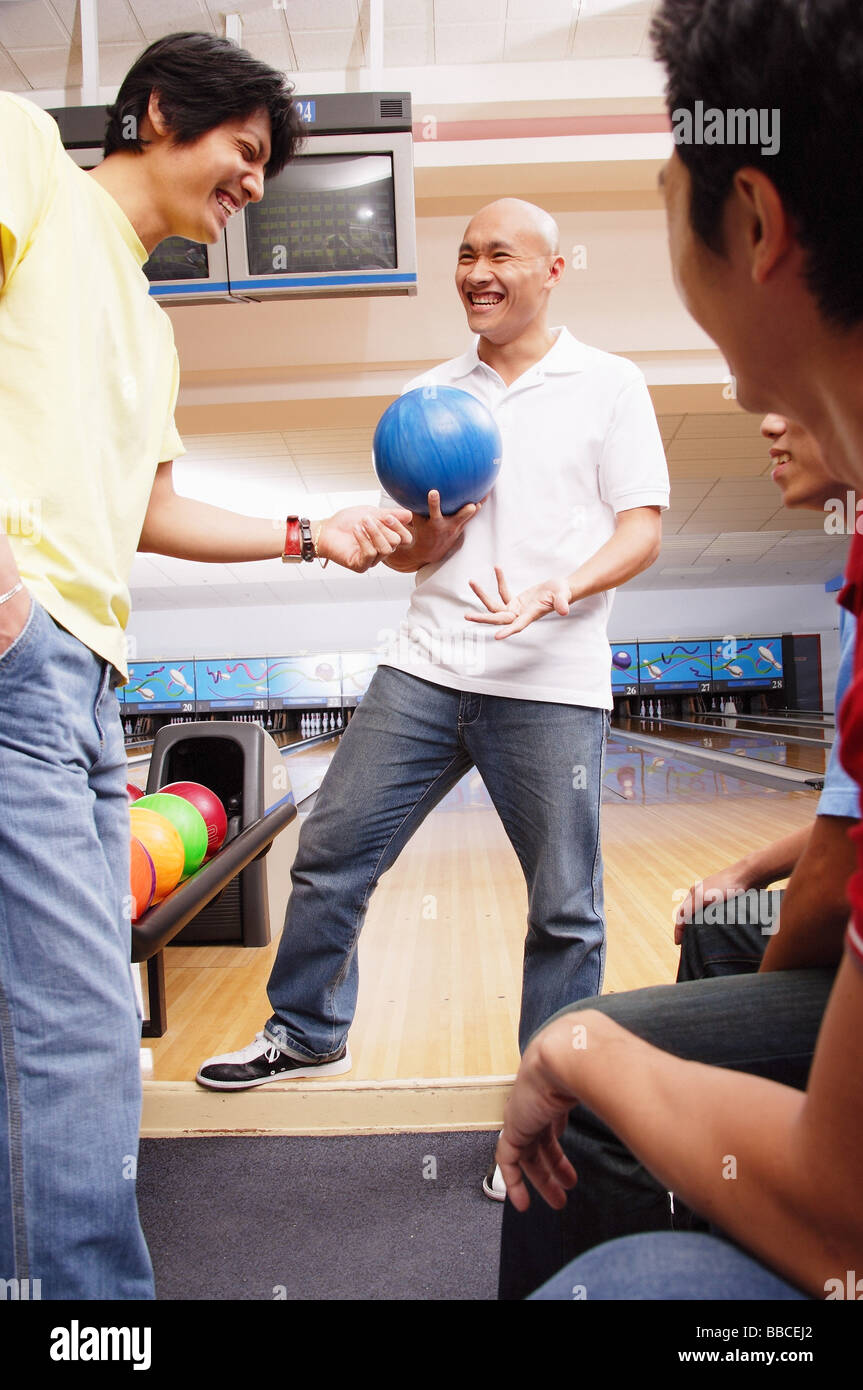 Mann, der Bowling-Kugel, umgeben von anderen Männern hält Stockfoto