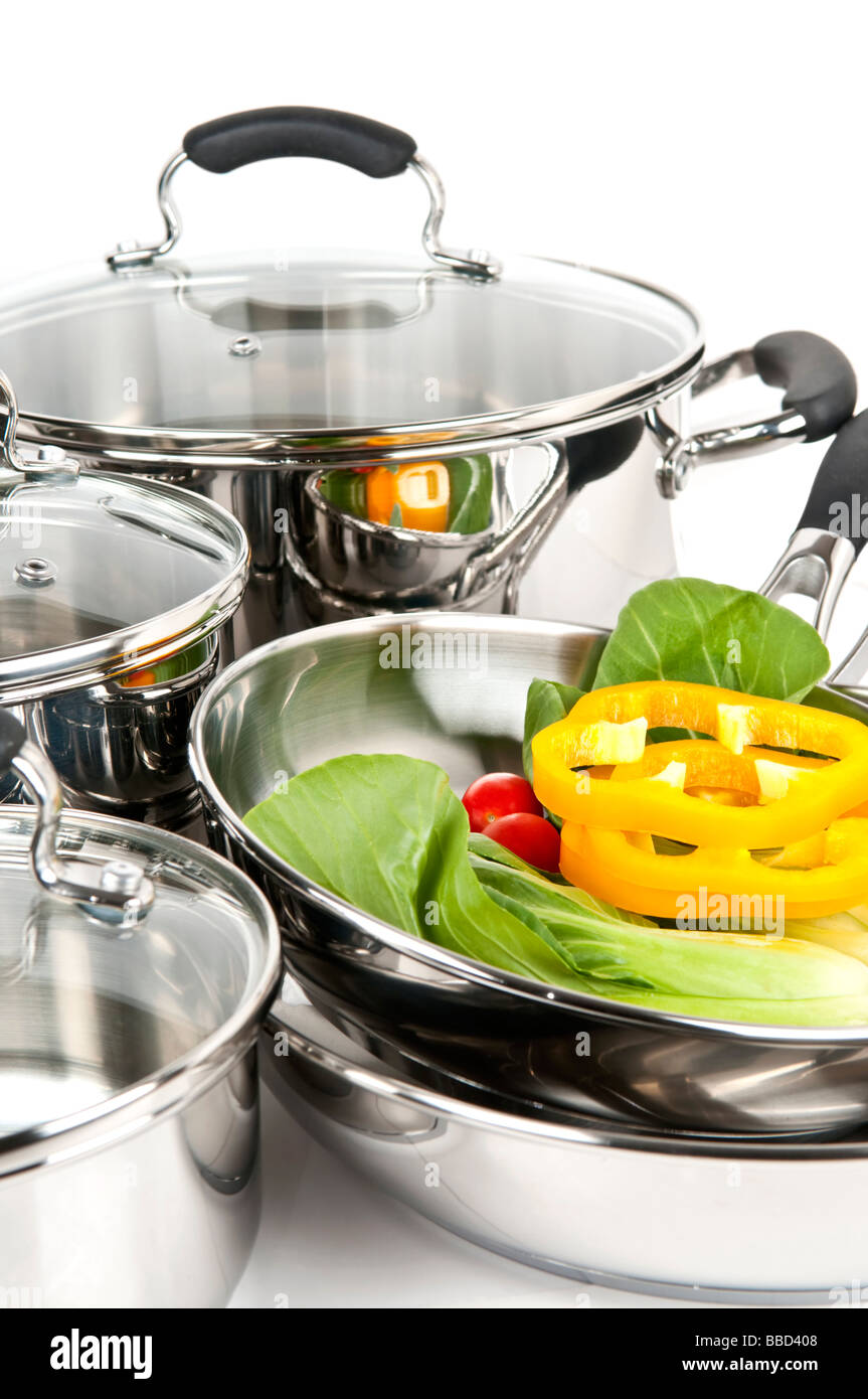 Edelstahl-Töpfe und Pfannen isoliert auf weißem Hintergrund mit Gemüse Stockfoto