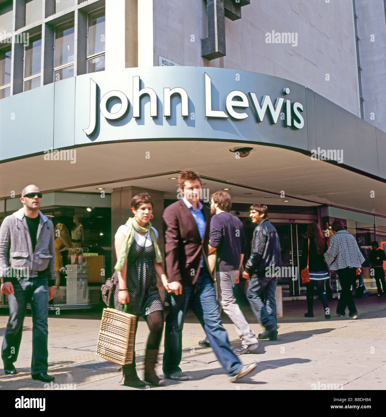 Shopper mit Tragetaschen zu Fuß hinter dem Eingang zu John Lewis Abteilung Speichern Oxford Street London England UK Stockfoto