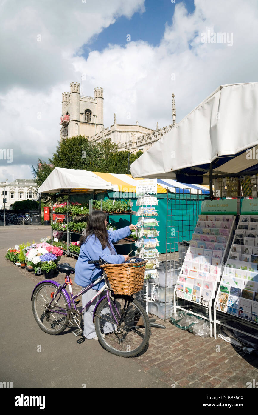 Eine Frau auf einem Fahrrad, die im Sommer an einem Marktstand in Cambridge, Großbritannien, Postkarten einkauft Stockfoto