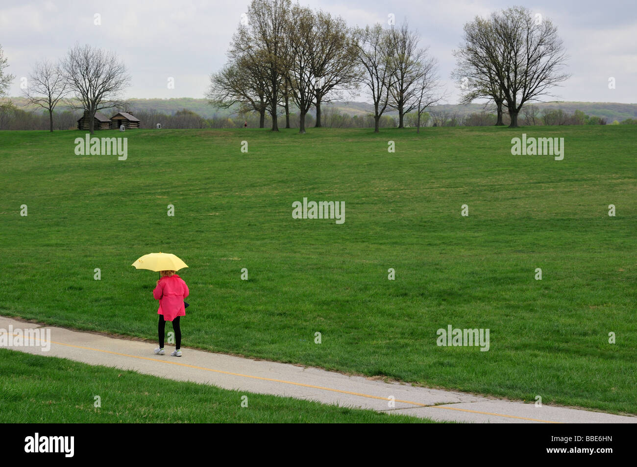 Eine Frau mit Regenschirm geht den asphaltierten Weg in Valley Forge National Historical Park Stockfoto
