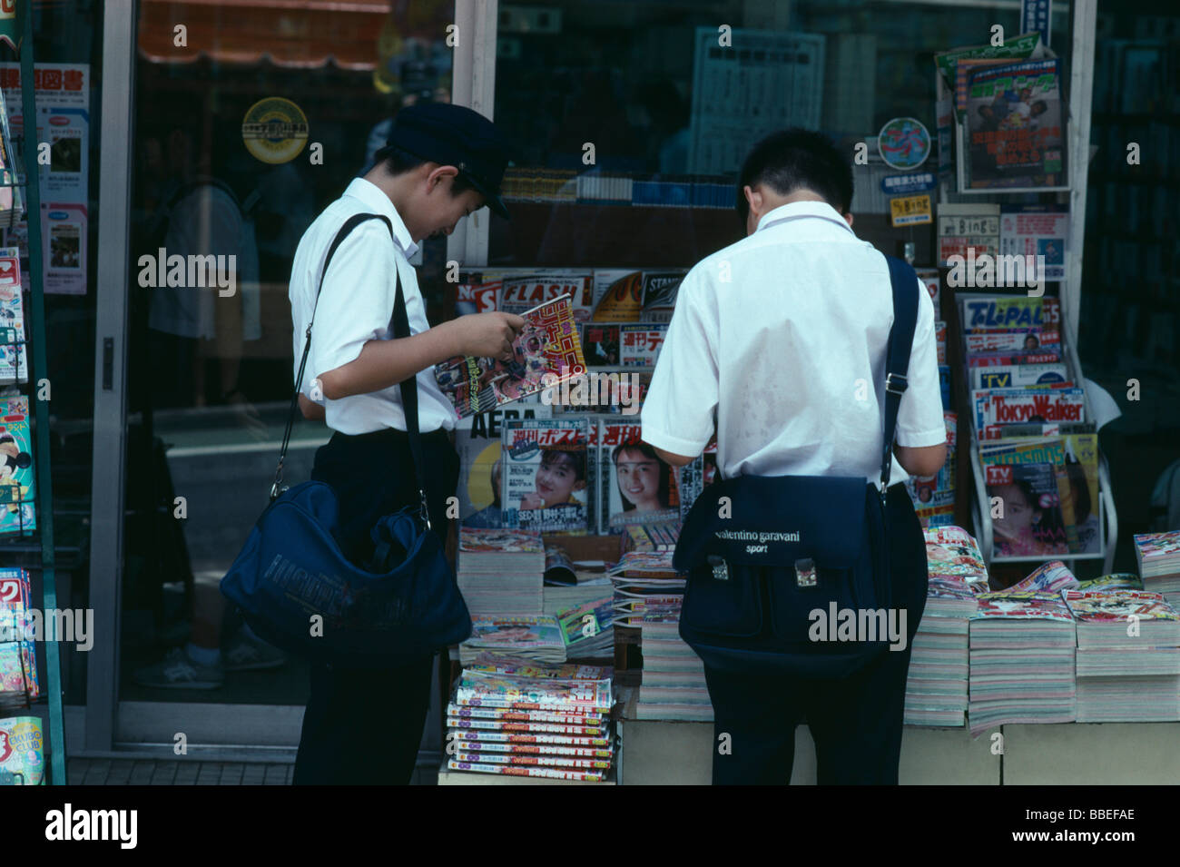 Chiba Narita zwei Junior hohe japanische Schüler in Uniform lesen Zeitschriften vom Bürgersteig Bürgersteig Stand JAPAN Stockfoto