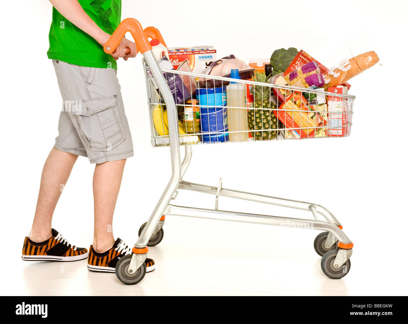 Nicht identifizierte Männer tragen Shorts und Sneaker, die den Einkaufskkarren des Supermarkts mit wöchentlichen Einkäufen auf weißem Hintergrund befüllen Stockfoto