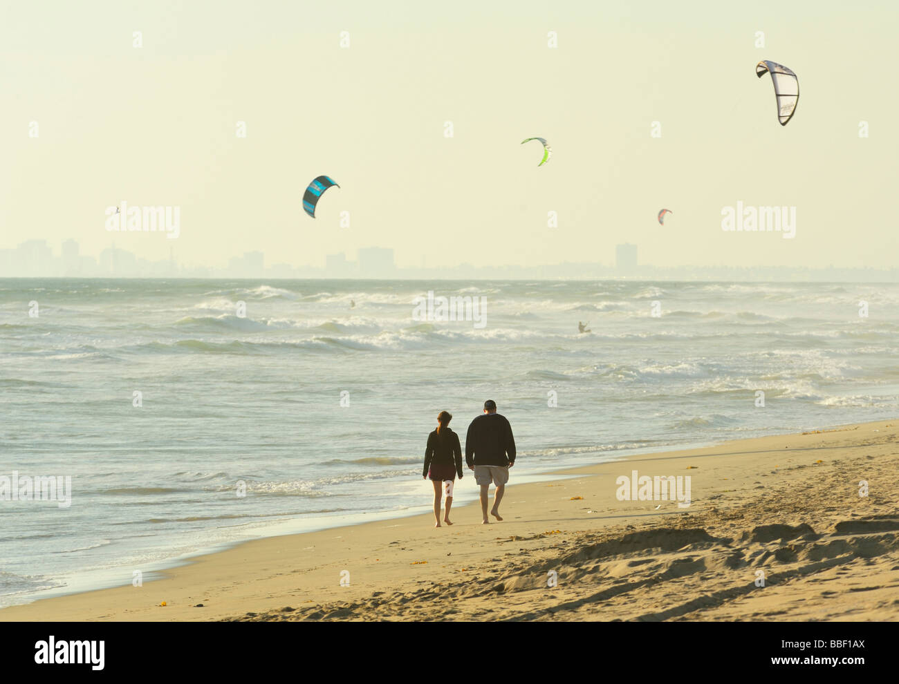 Wandern am Strand mit Kite-Surfern vor der Skyline von Long Beach, Huntington Beach CA Stockfoto