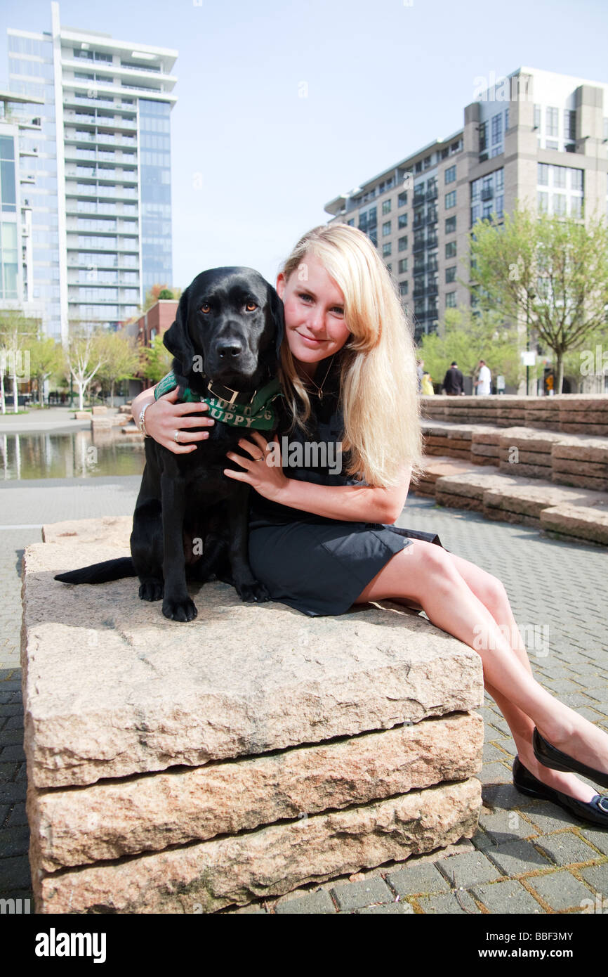 Blondine mit weißen kaukasischen Frau mit schwarzen Labrador Guide Hund in eine urbane Parklandschaft. Stockfoto