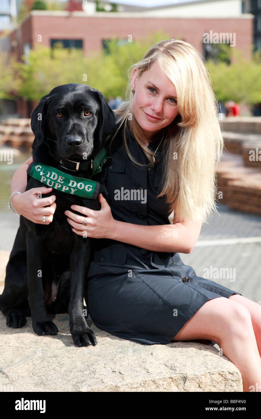 Blondine mit weißen kaukasischen Frau mit schwarzen Labrador Guide Hund in eine urbane Parklandschaft. Stockfoto