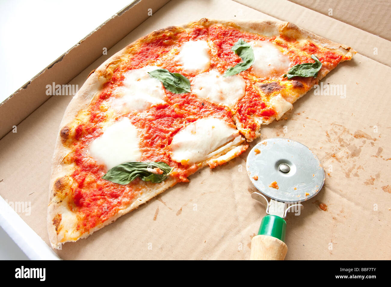 Margherita Pizza in Box mit Pizzaschneider, Basilikumbelag. Stockfoto
