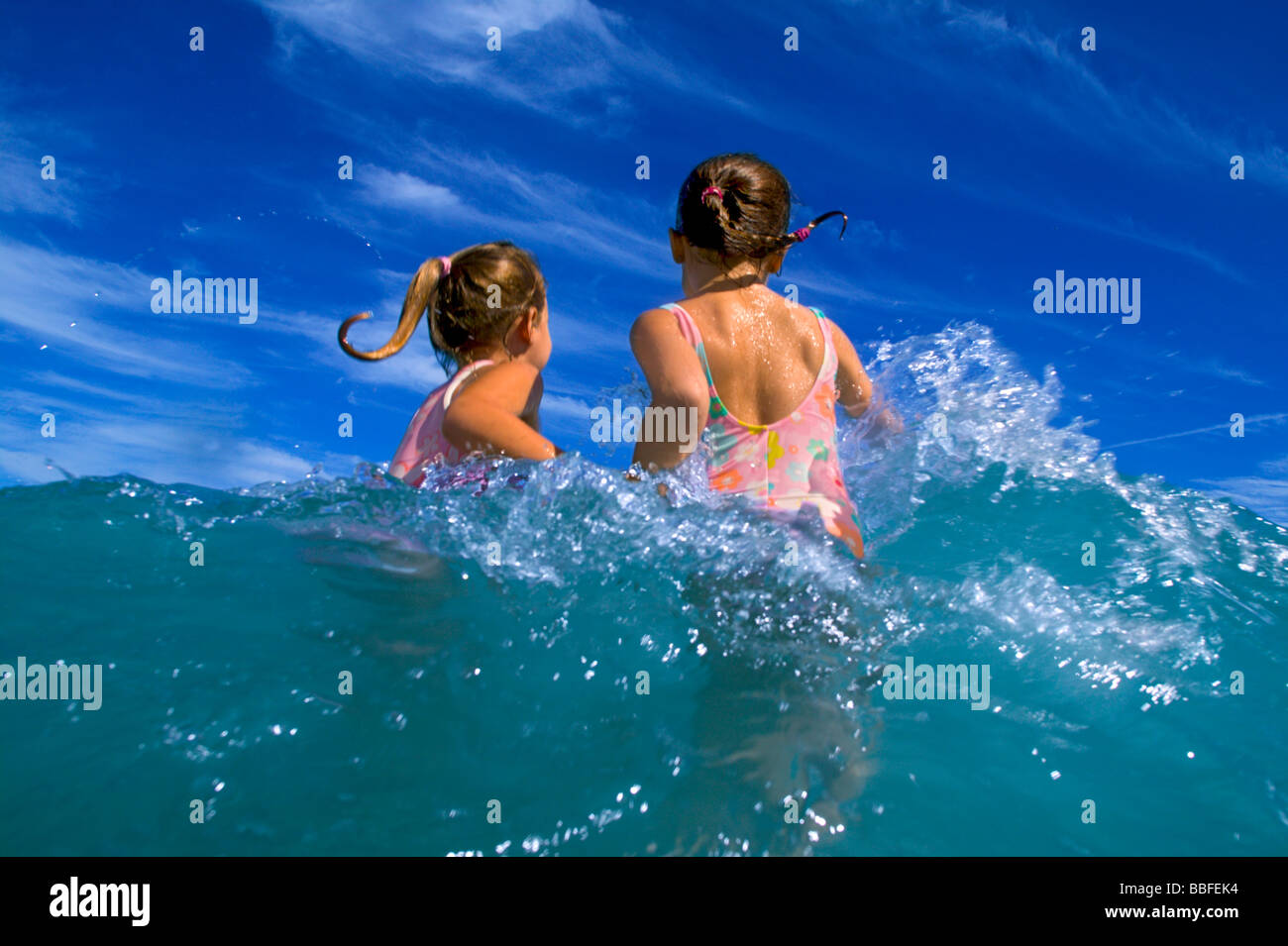 Zwei junge Mädchen spielen in den Wellen des Ozeans mit blauem Himmel. Dieses Bild hat viel Bewegungsunschärfe, so dass die Mädchen nicht 100 % scharf sind. Stockfoto