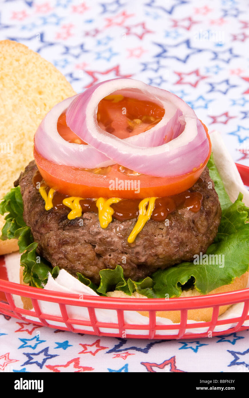 Eine Nahaufnahme von einem saftigen Hamburger mit Tomaten-Zwiebel-Senf und Ketchup auf einem patriotischen 4. Juli Hintergrund Stockfoto