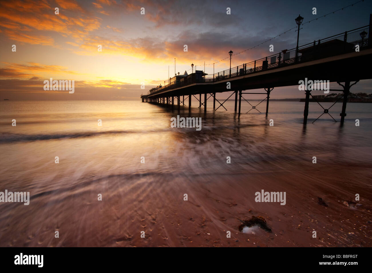 Wellen über den Strand bei Sonnenaufgang über Paignton Pier an der englischen Riviera Küste in Paignton in Devon UK Stockfoto