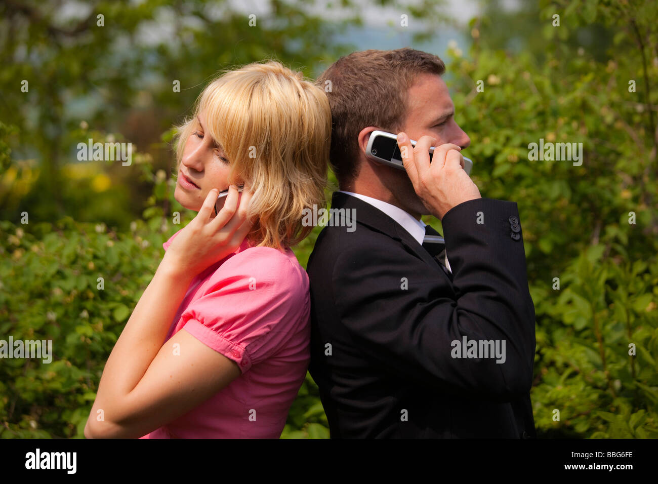 Junge Frau und ein junger Mann stehen Rücken an Rücken während des Gesprächs auf dem Handy Stockfoto