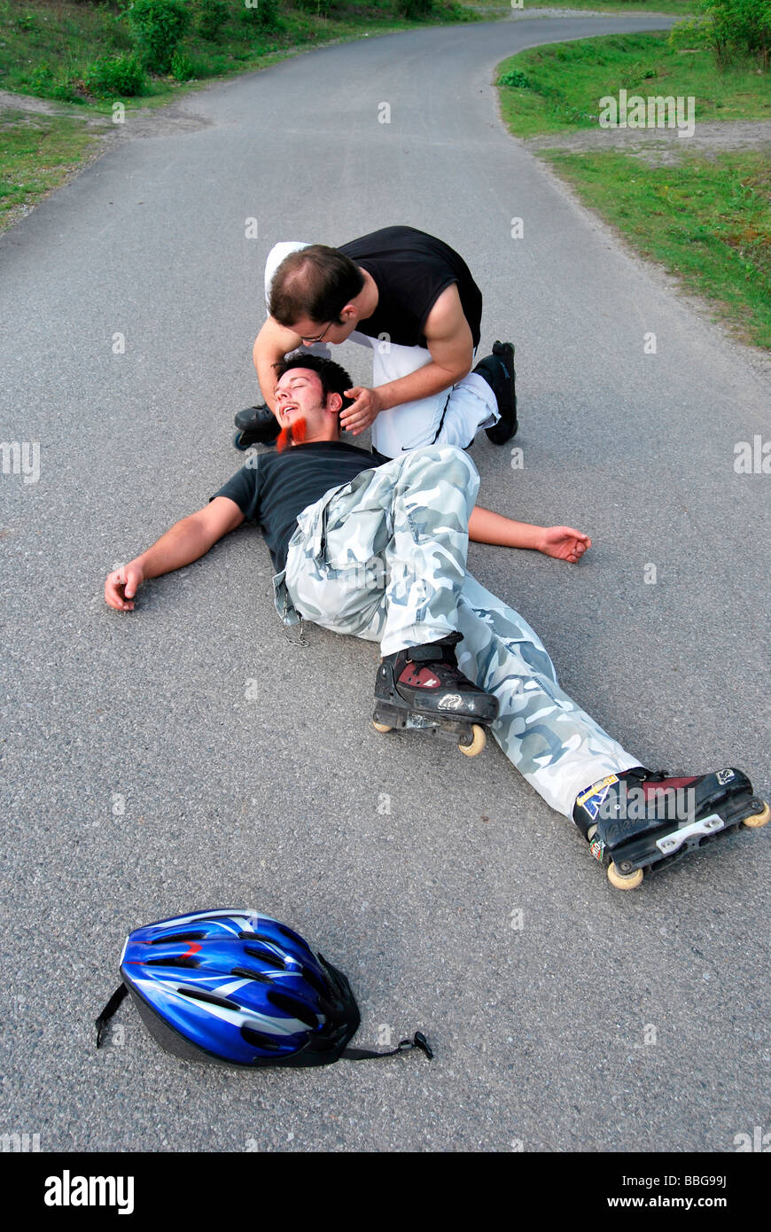 Erste Hilfe, Inline-Skater auf dem Boden nach Sturz, bewegungslos, Person, die hilft Stockfoto