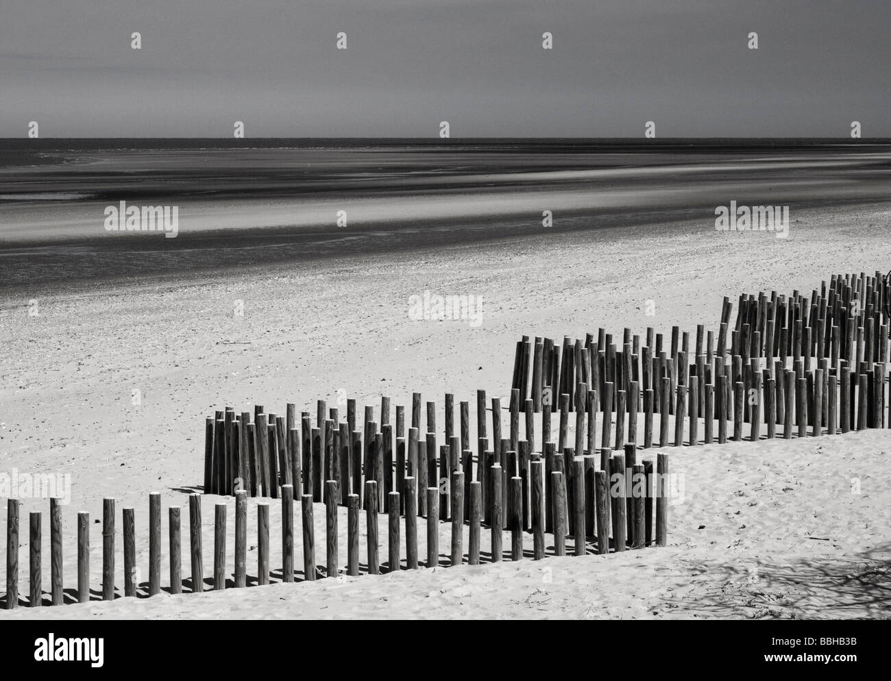 Ein monochromes Bild eine hölzerne Leiste an einem Sandstrand mit der Flut Stockfoto