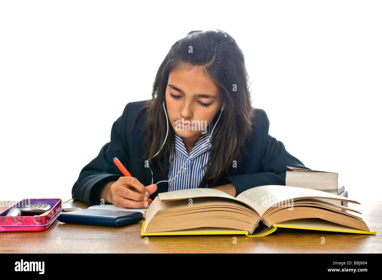 Horizontale Porträt des jungen Schulmädchen in ihrer Uniform sitzt am Schreibtisch ihre Hausaufgaben während auf ihrem Ipod hören Stockfoto