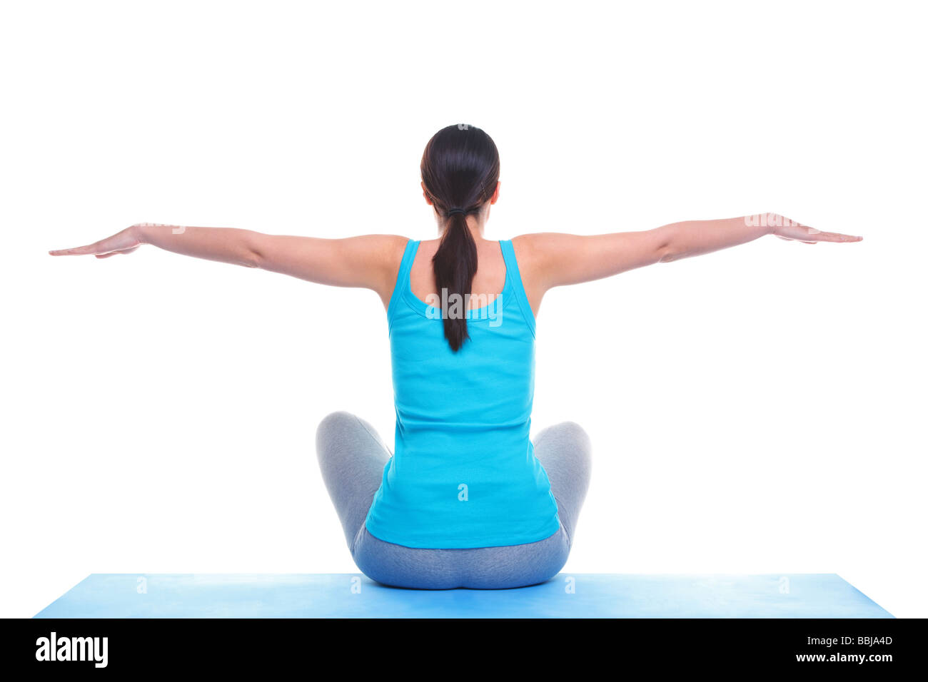 Rückansicht einer Brünette Frau setzte sich auf eine Yoga-Matte mit ihren Armen heraus in einem ausgeglichenen Stockfoto