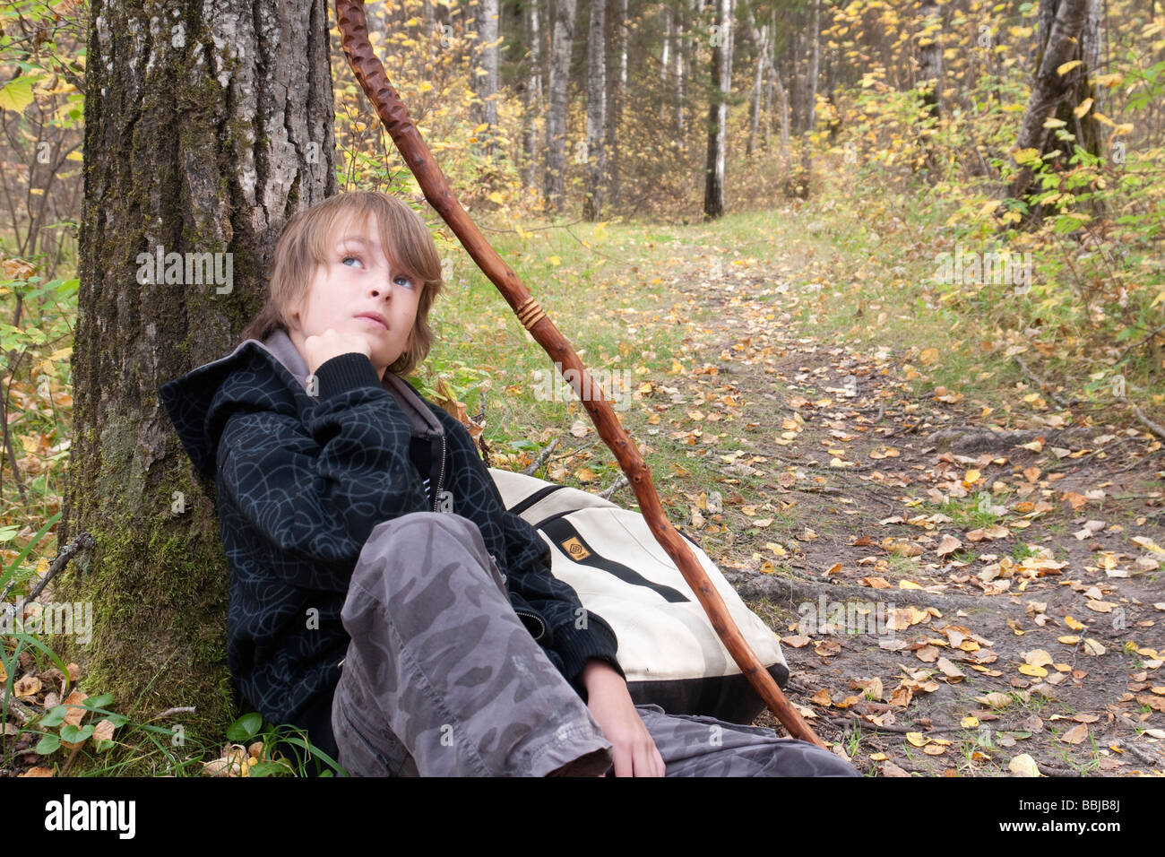 Zehn Jahre alter Junge sitzt stützte sich auf Baum neben Trail, See Katherine Riding Mountain National Park, Manitoba Stockfoto