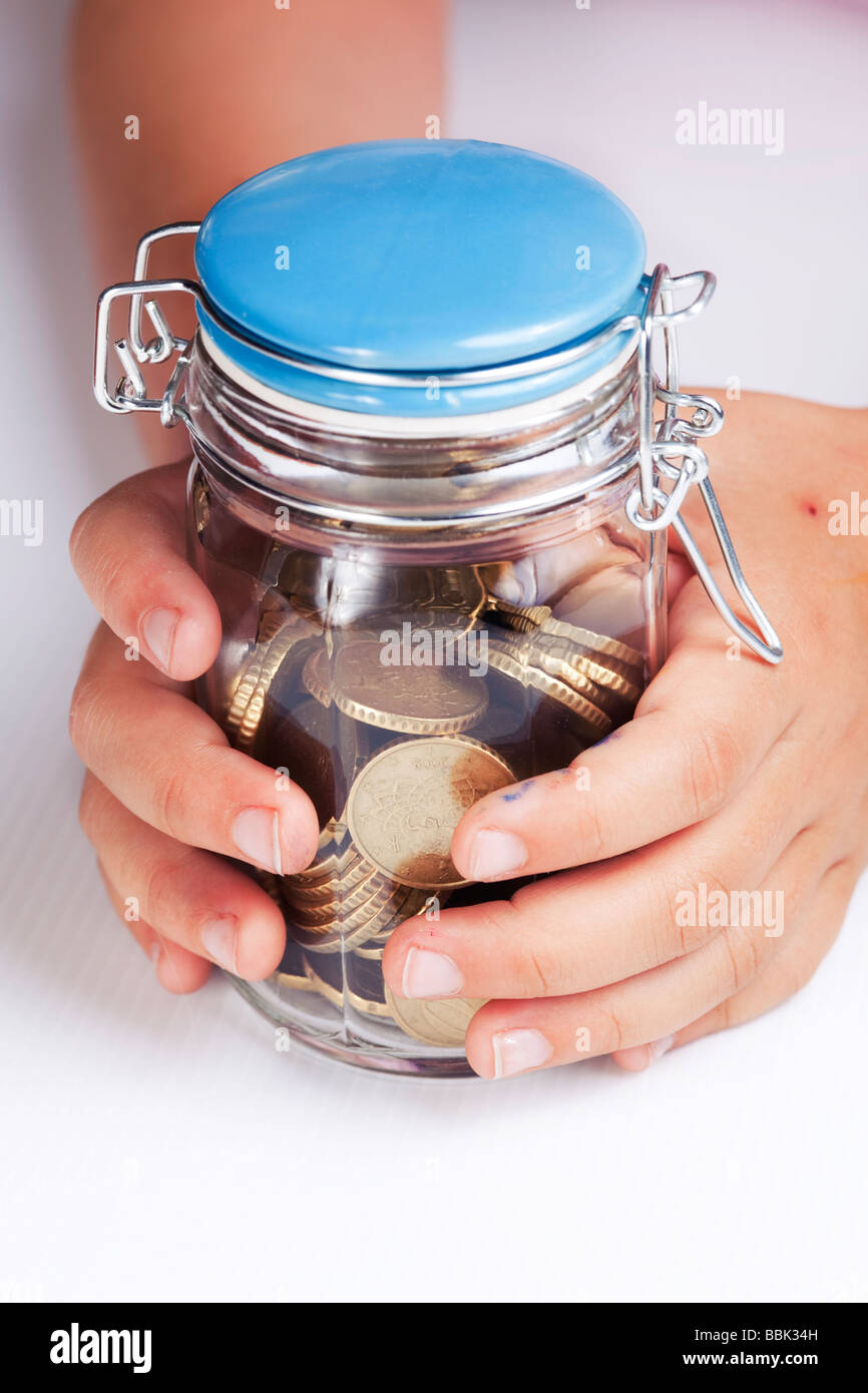 die Hände des Kindes um ein Glas voller Münzen Stockfoto