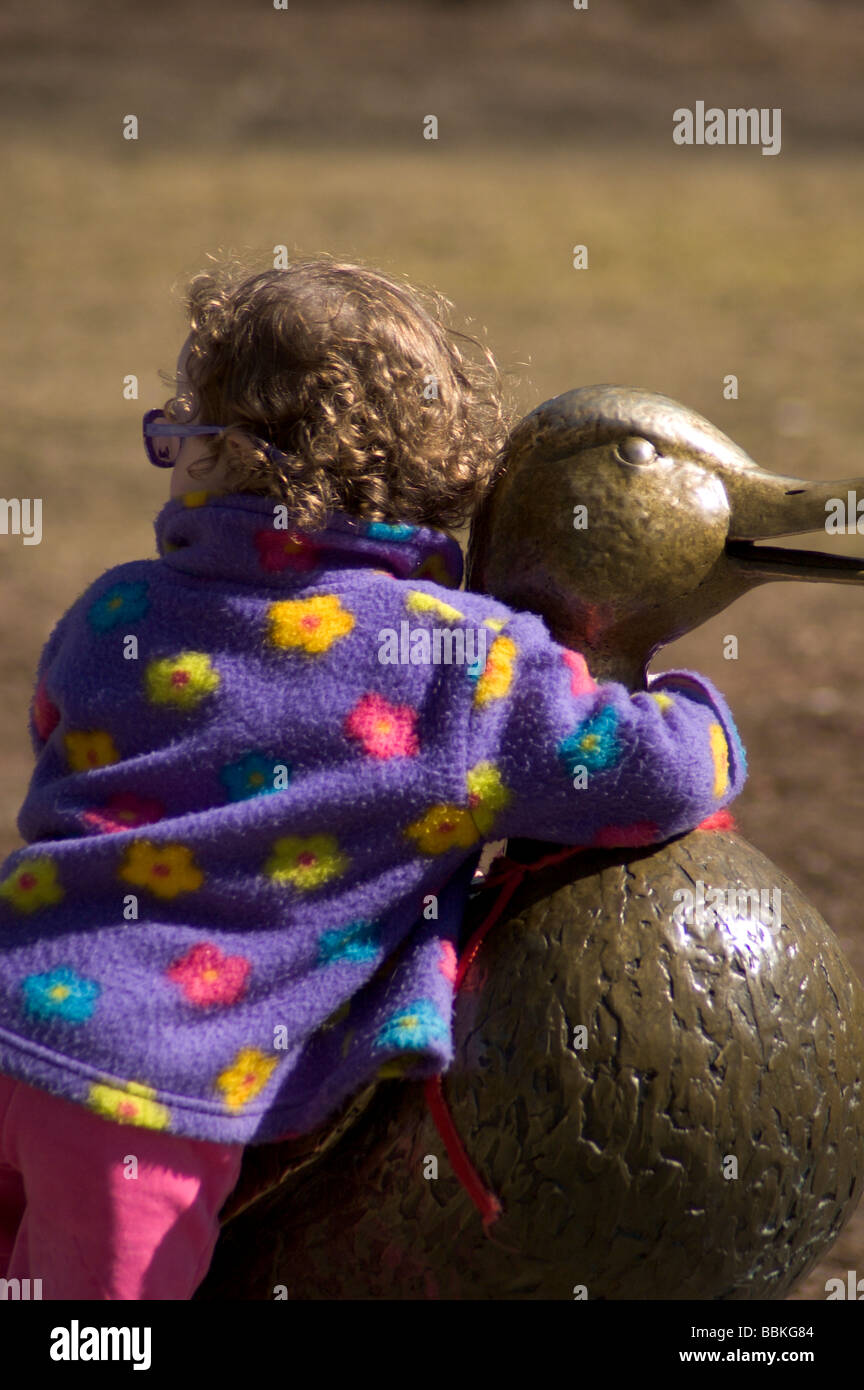Kleines Mädchen mit Sonnenbrille umarmt die Bronzestatue der Mutter Ente in der Boston Public Gardens. -Boston MA, Vereinigte Staaten Stockfoto