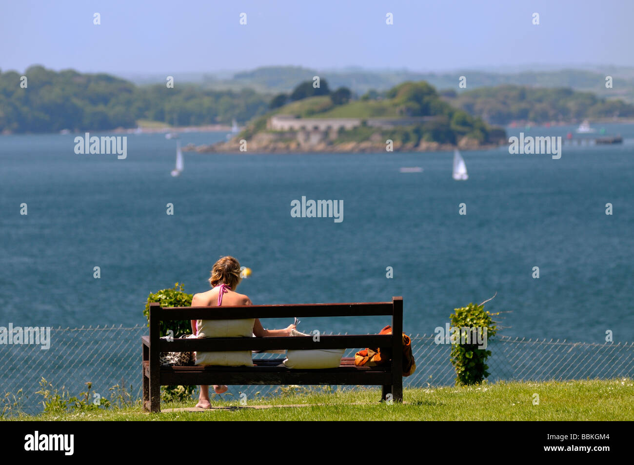 Einsame Frau sitzt auf der Parkbank mit Blick aufs Meer Entfernung verschwimmen Plymouth sound Stockfoto