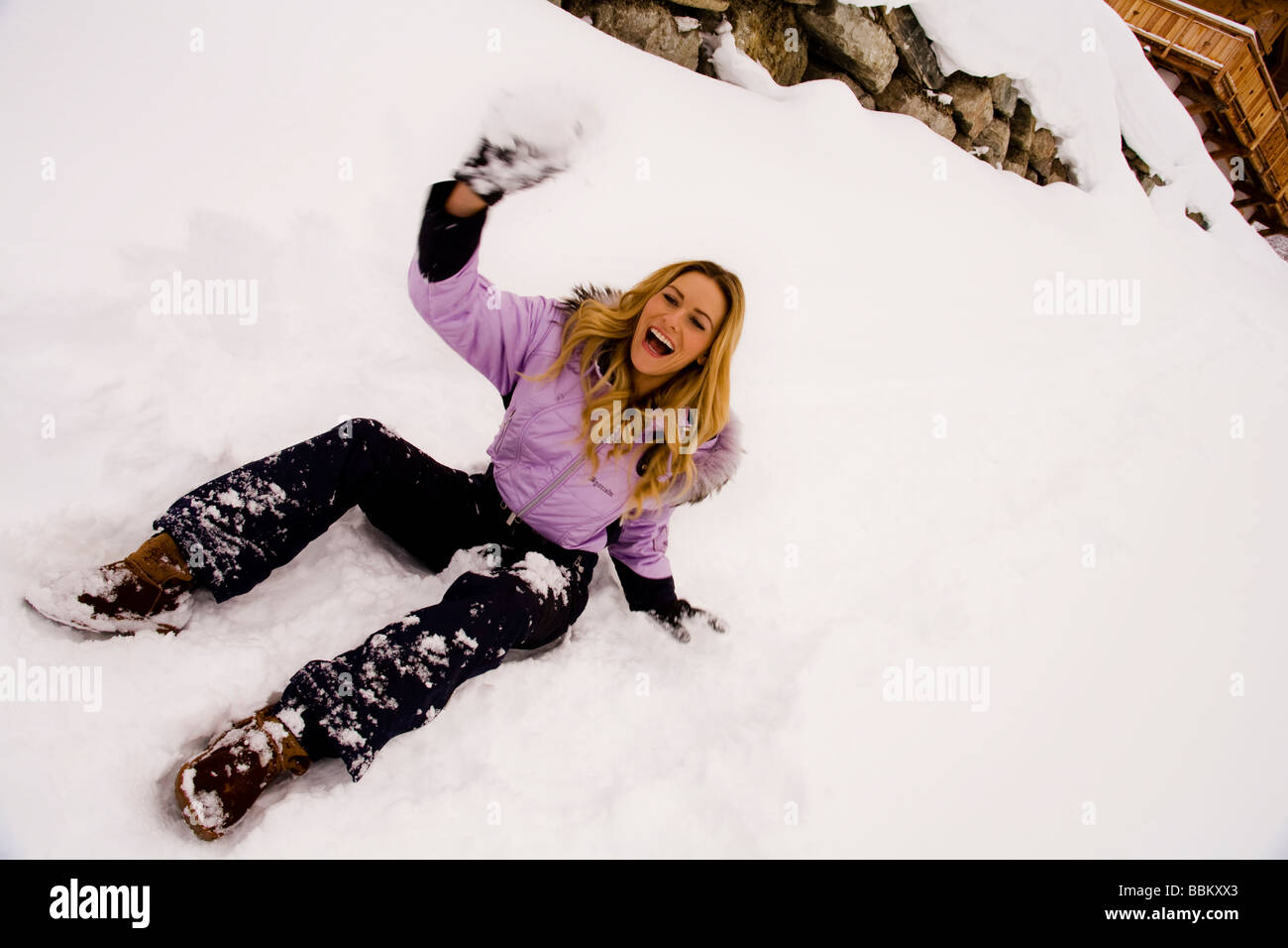 Eine junge, blonde Frau sitzt in den Schnee und wirft Schneebälle, die eine schöne Zeit. Stockfoto