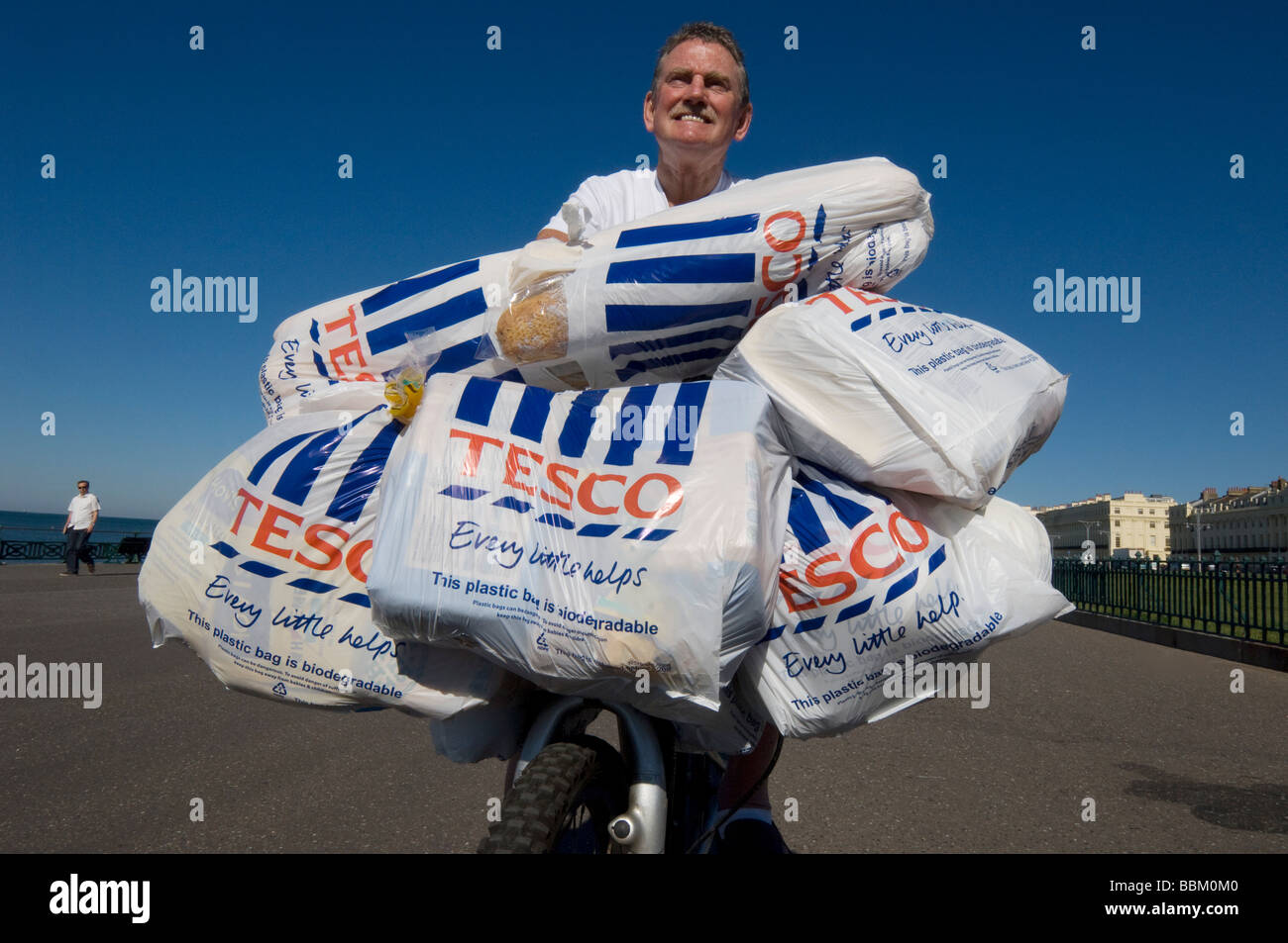 Ein Mann kommt zurück vom Einkaufszentrum Tesco auf einem Fahrrad mit beladen mit Plastiktüten voller Lebensmittel. Stockfoto