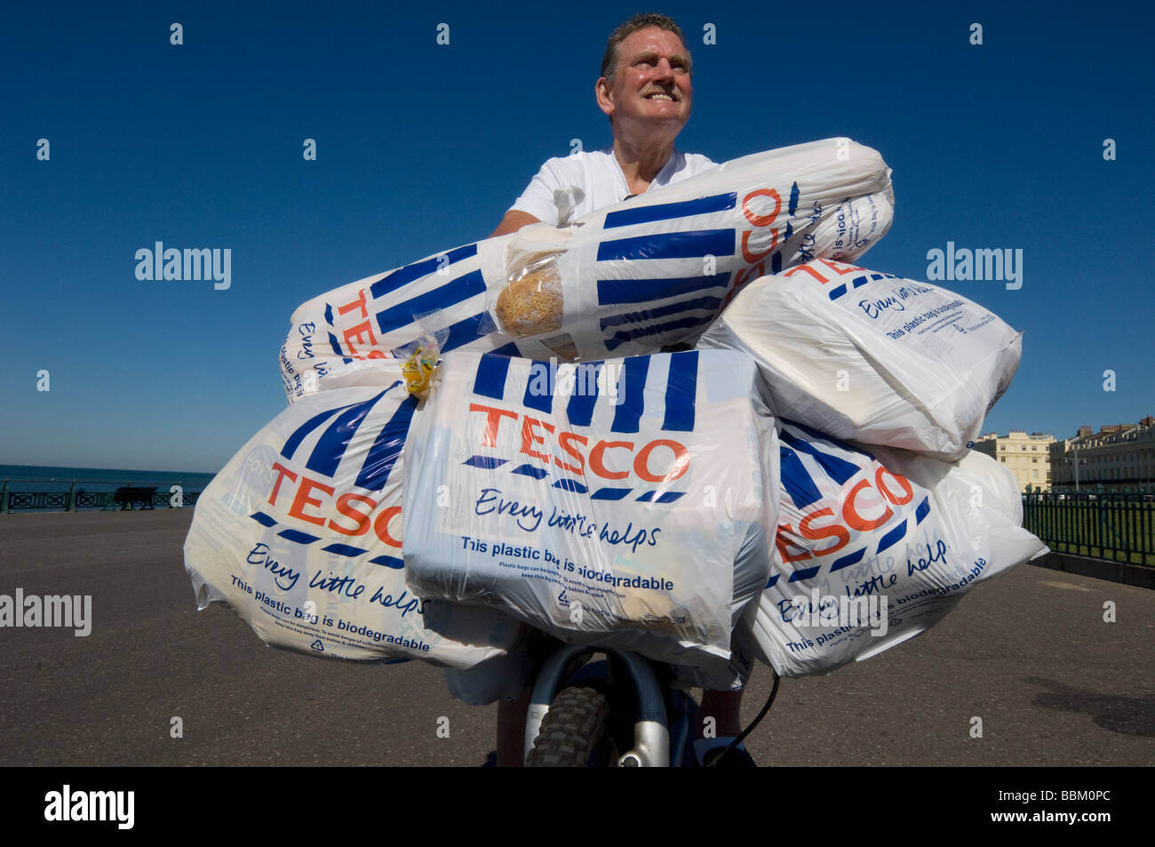 Ein Mann kommt zurück vom Einkaufszentrum Tesco auf einem Fahrrad mit beladen mit Plastiktüten voller Lebensmittel. Stockfoto