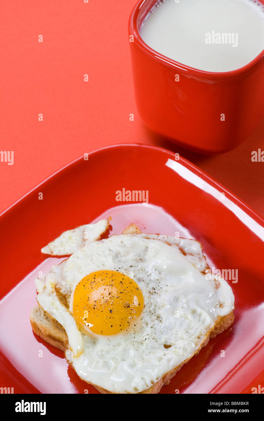 Frühstück, Tasse Milch, Spiegelei, gewürzt mit Salz und Pfeffer auf rote Geschirr Stockfoto