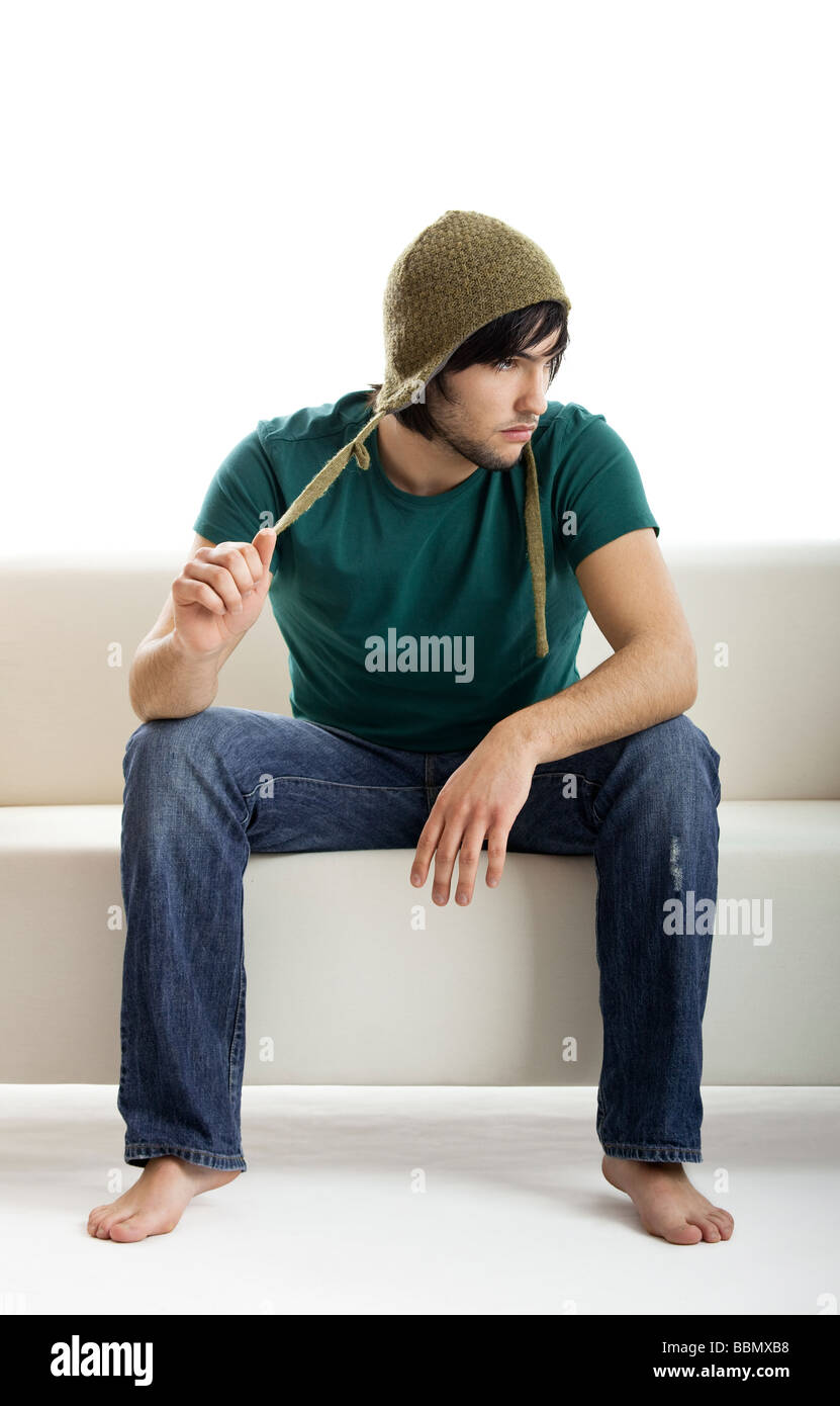 Gut aussehender junger Mann sitzt auf der Couch, isoliert auf weiss Stockfoto