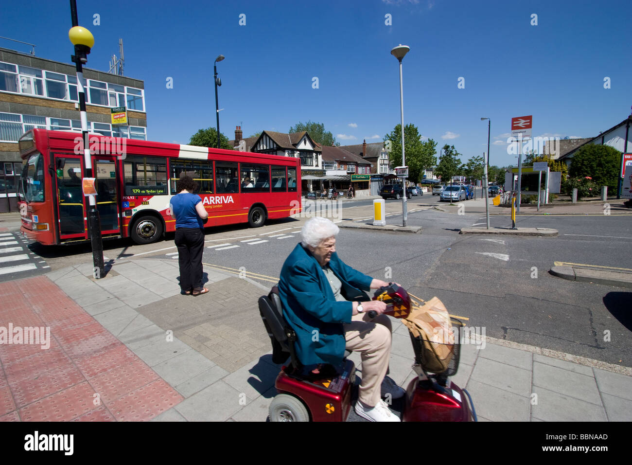 Straßenszene in Chingford London auf Essex Grenze mit ältere Frau auf Motorbility Scooter Rollstuhl mit Bus powered Stockfoto