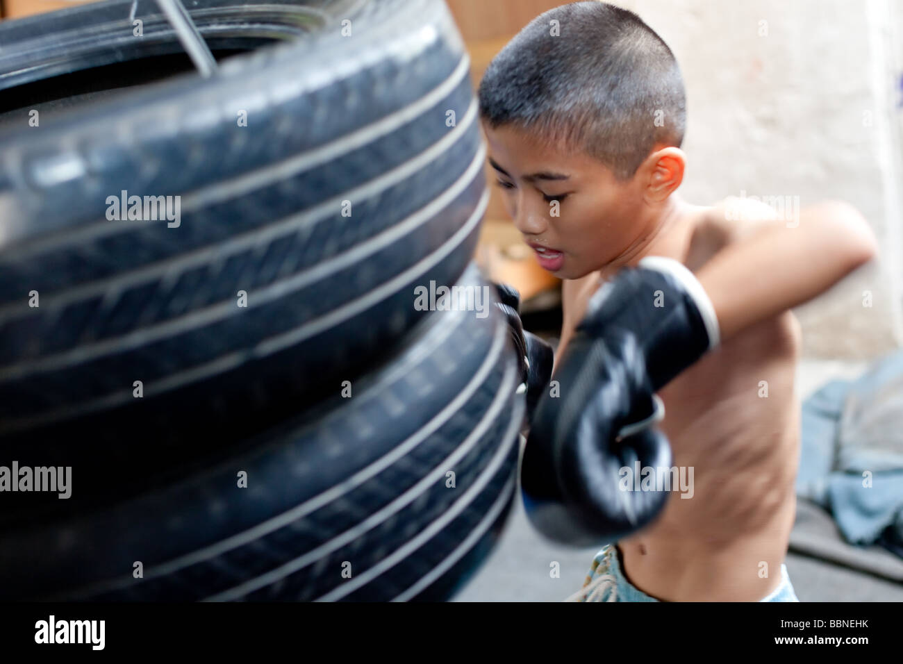 Junge skinny Muay thai Boxer Züge mit Reifen in einem Slum Camp leichte Bewegungsunschärfe mit Einfrieren flash Stockfoto