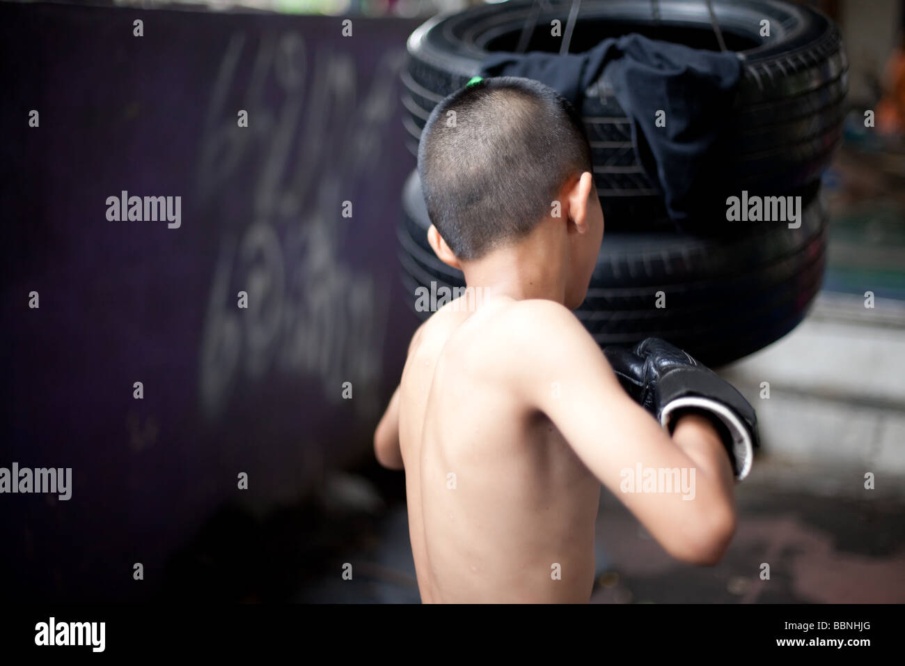 Junge skinny Muay thai Boxer Züge mit Reifen in einem Slum Camp leichte Bewegungsunschärfe mit Einfrieren flash Stockfoto