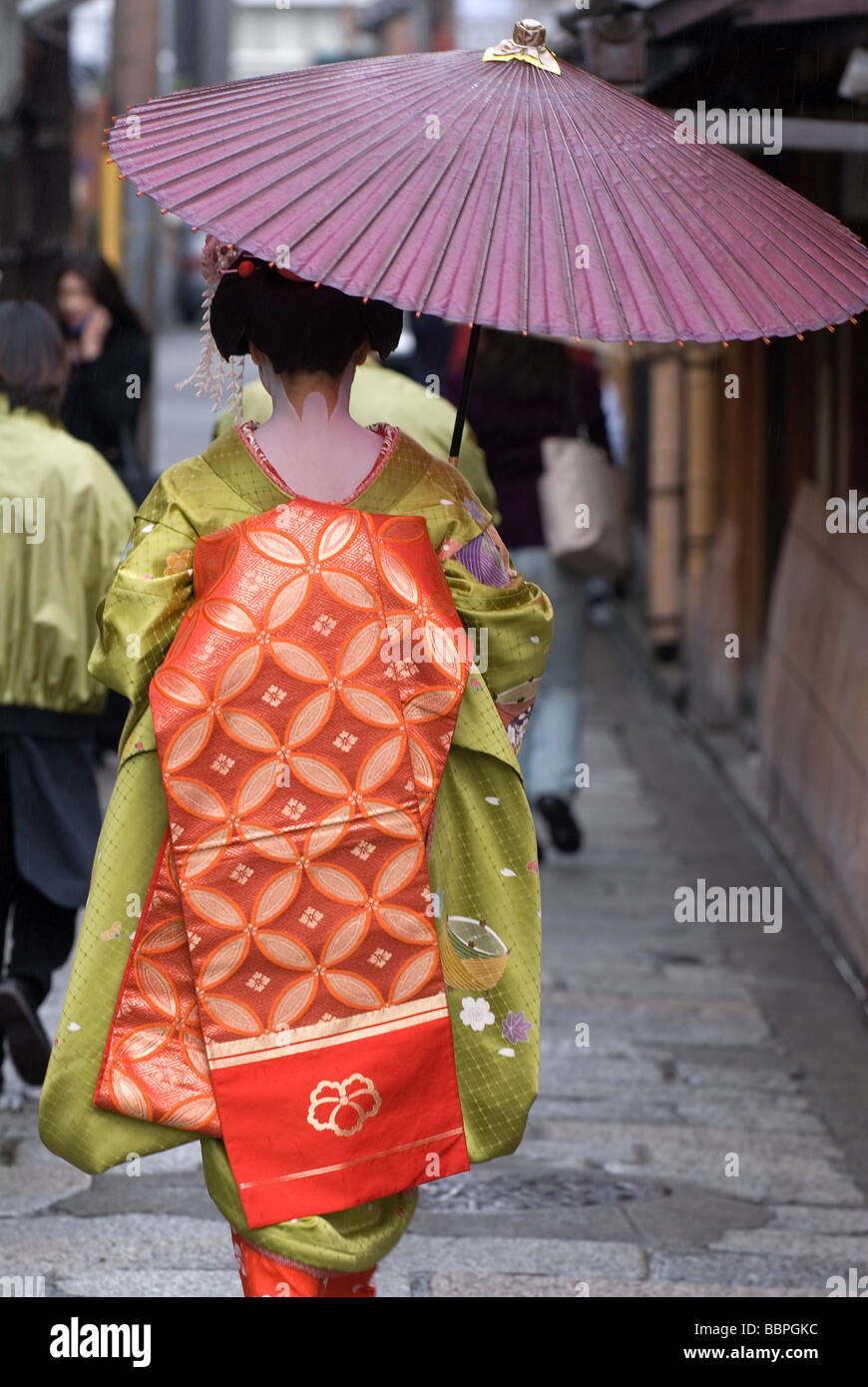 Eine Lehrgeisha oder Maiko, die auf einer Seitenstraße im Stadtteil Gion hanamachi in Kyoto mit einem Regenschirm spaziert, Kyoto, Japan. Stockfoto