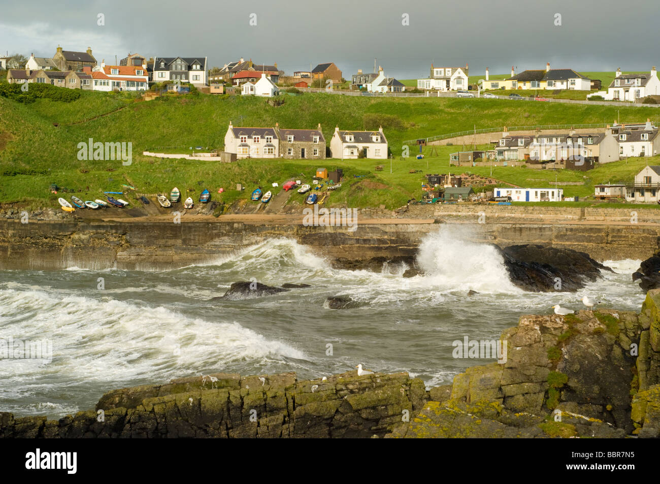 Stürmische Wellen in dem traditionellen Fischerdorf und Hafen von Stonehaven, Schottland. Die Felsen sind aus Granit. Stockfoto