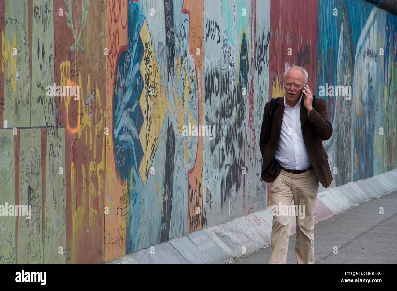 Ein Fußgänger, der mit dem Handy unterwegs ist, während er die Gedenkstätte der East Side Gallery auf dem verbleibenden Teil der Berliner Mauer entlang geht. Deutschland Stockfoto