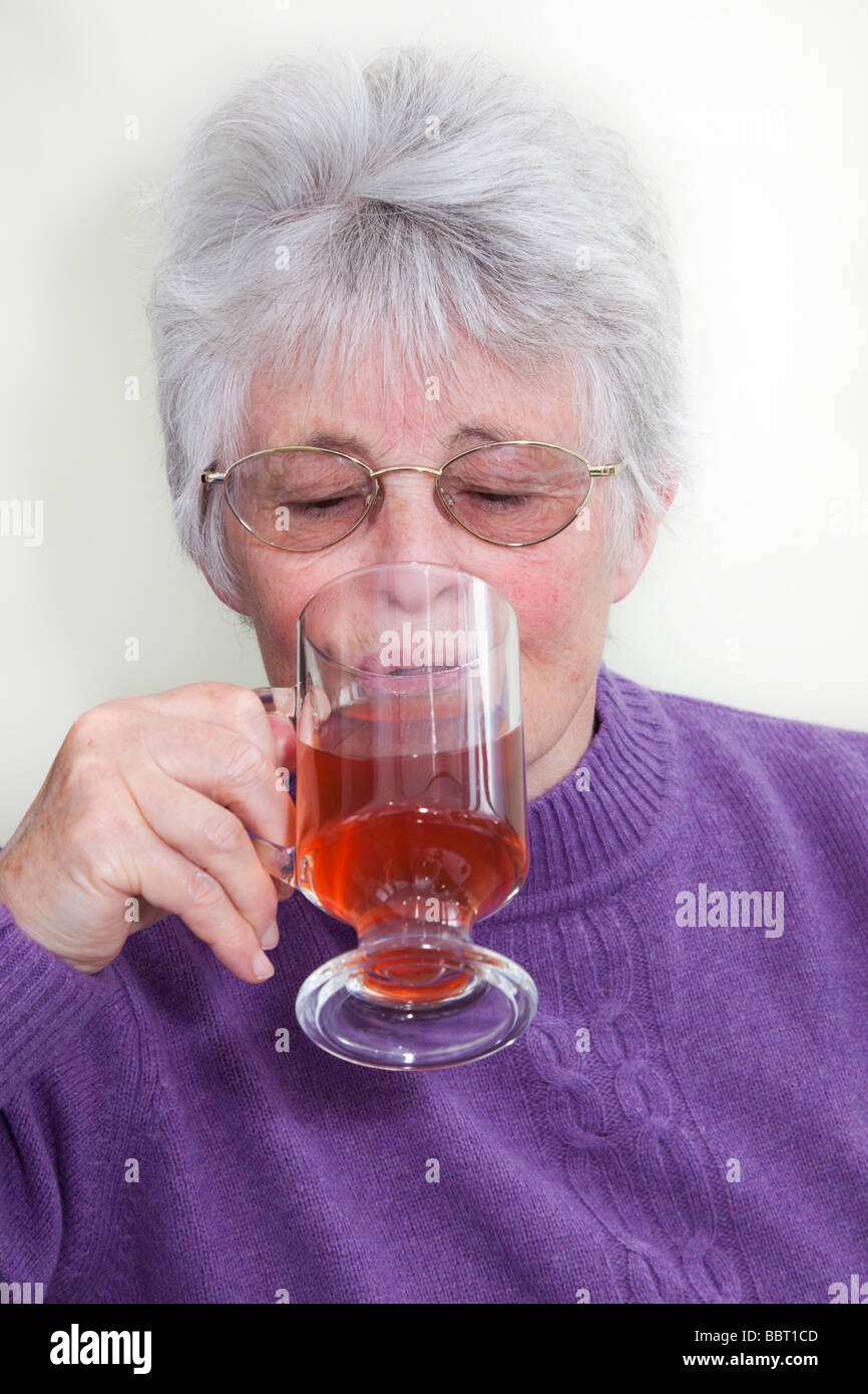 Ältere ältere Frau OAP Dame trägt ein lila Jumper und Trinken rote Früchte Tee in einem Glas mug. England Großbritannien Großbritannien Stockfoto