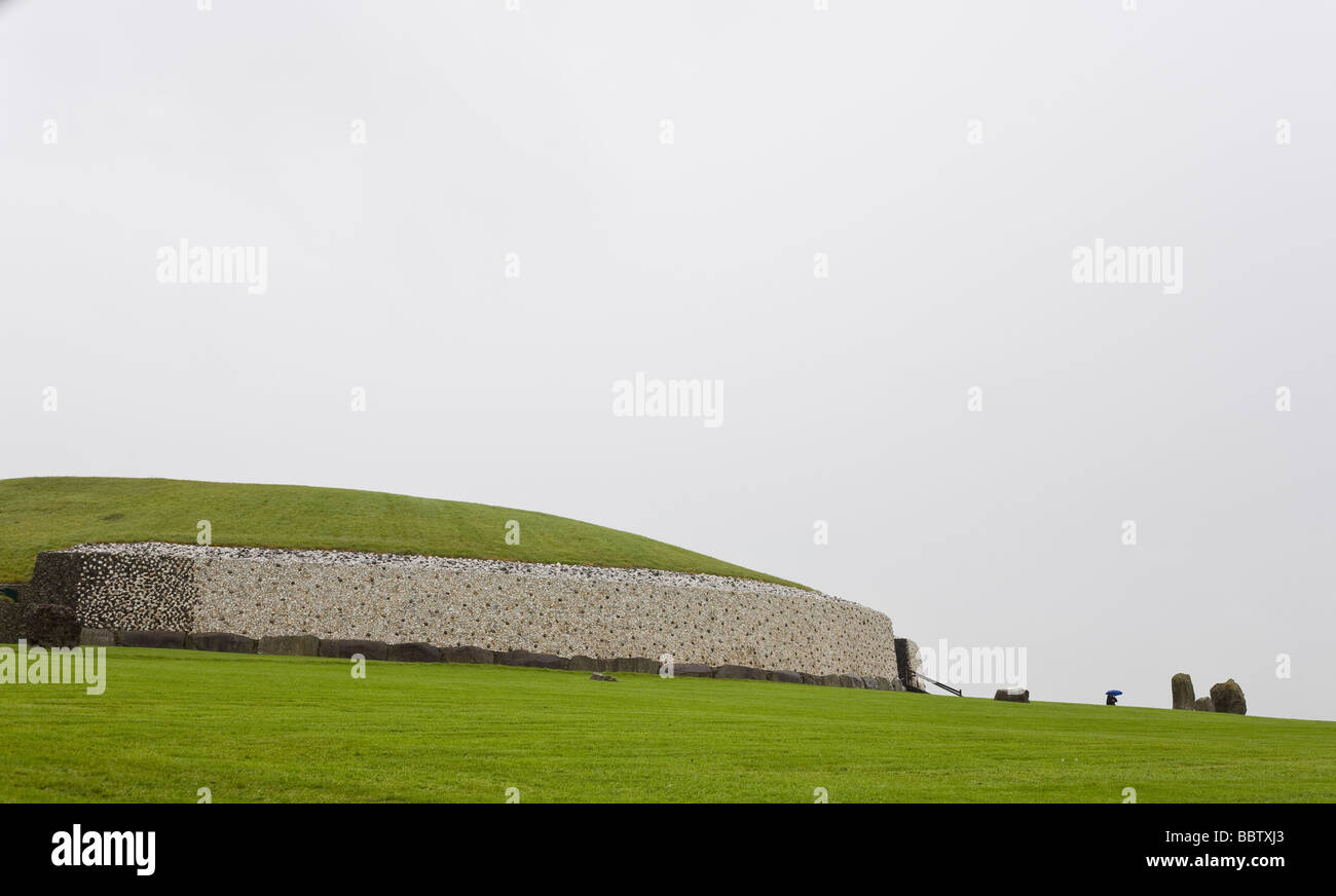 Warten auf die nächste Tour von Newgrange. Ein Reiseleiter mit einem blauen Schirm steht neben der großen Mauer und Hügel von Newgrange. Stockfoto