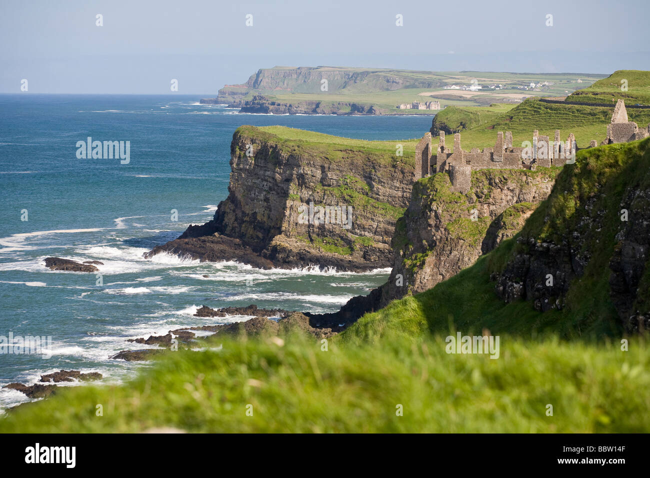 Dunluce am Rande. Die Ruine des Dunluce Castle als es schlüpft in das Meer, inmitten im grünen der wunderschönen Küste von Antrim. Stockfoto