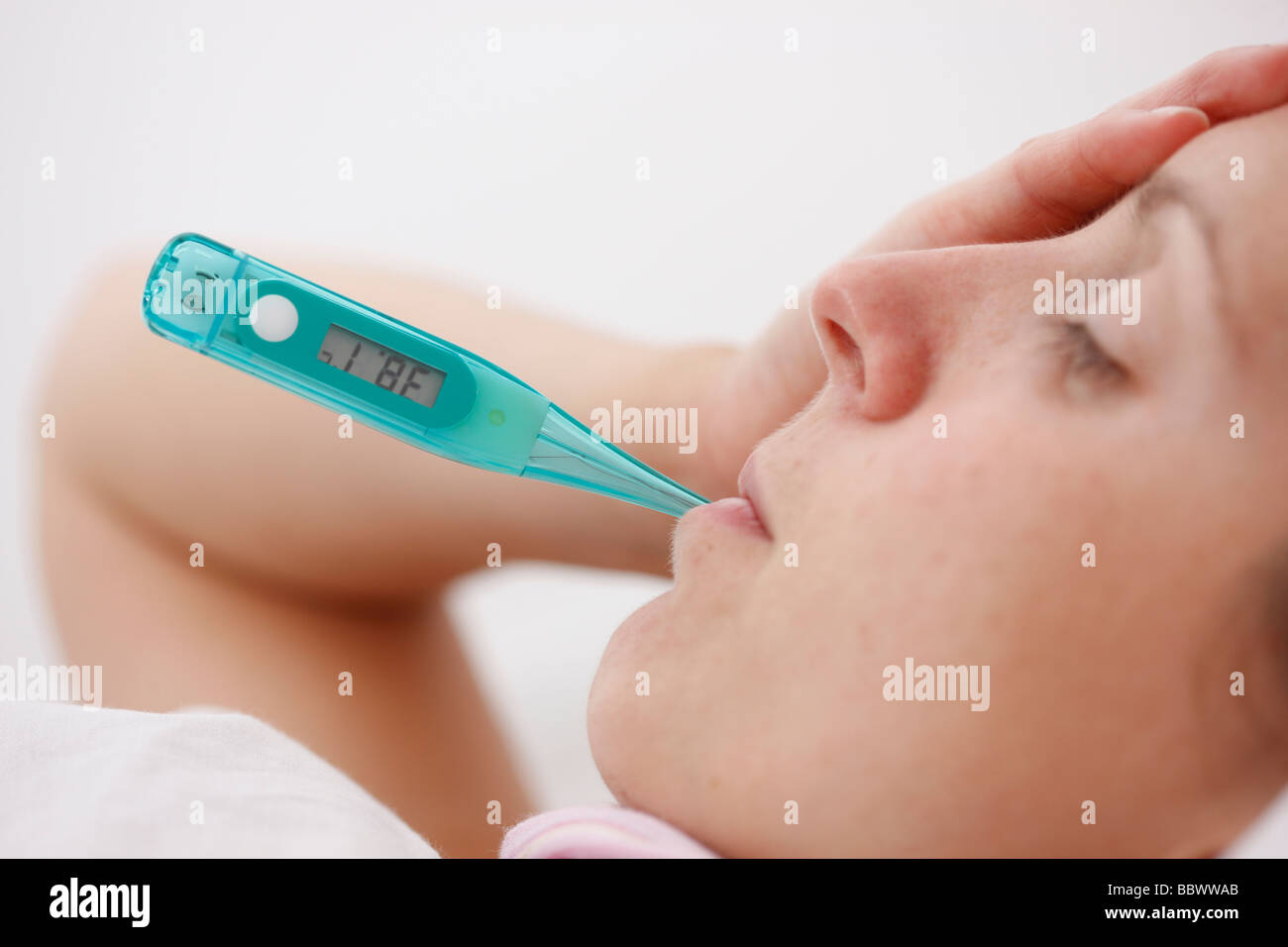 Frau zu Hause krank mit Fieber im Bett, verwendet ein Fieberthermometer für die Messung der Körpertemperatur. Stockfoto
