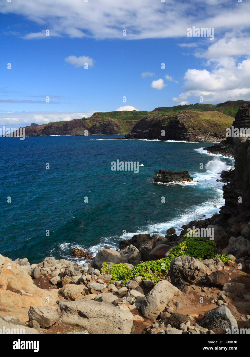 Surfen Sie, bricht der felsigen nördlichen Küste Maui mit Montain Palette und blauer Himmel mit leichten Wolken im Hintergrund Stockfoto