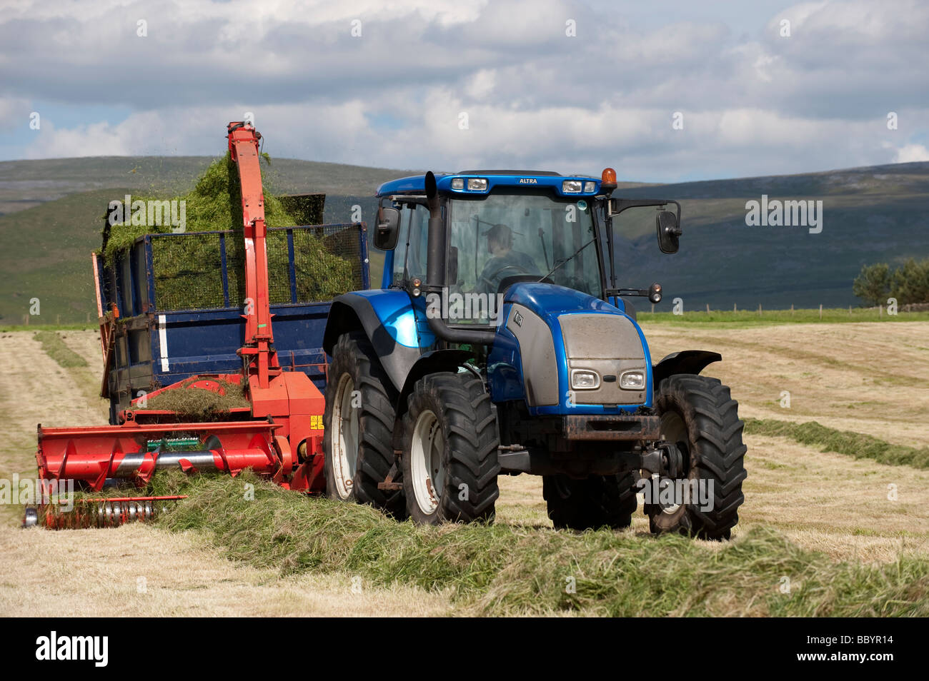 Valtra-Traktor zieht einen Kverneland Feldhäcksler mit Anhänger Silageherstellung für das Vieh Cumbria, England Stockfoto