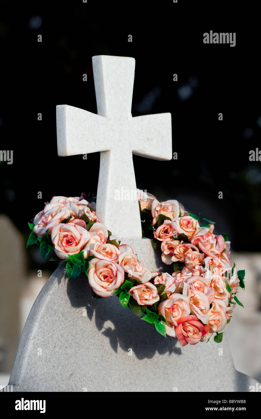 Ein Kreuz auf einem Grabstein mit einem Kranz von Blumen geschmückt Stockfoto