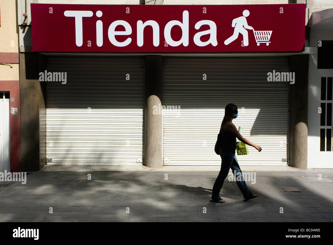 Ein Mädchen trägt eine Maske geht auf der Straße vor einem geschlossenen Geschäft in Mexiko-Stadt, DF, Mexiko. Stockfoto