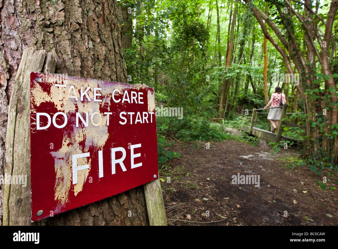 Frau geht vorbei an einem Hinweisschild kümmern tun nicht Start Fire auf einem Waldspaziergang Stockfoto