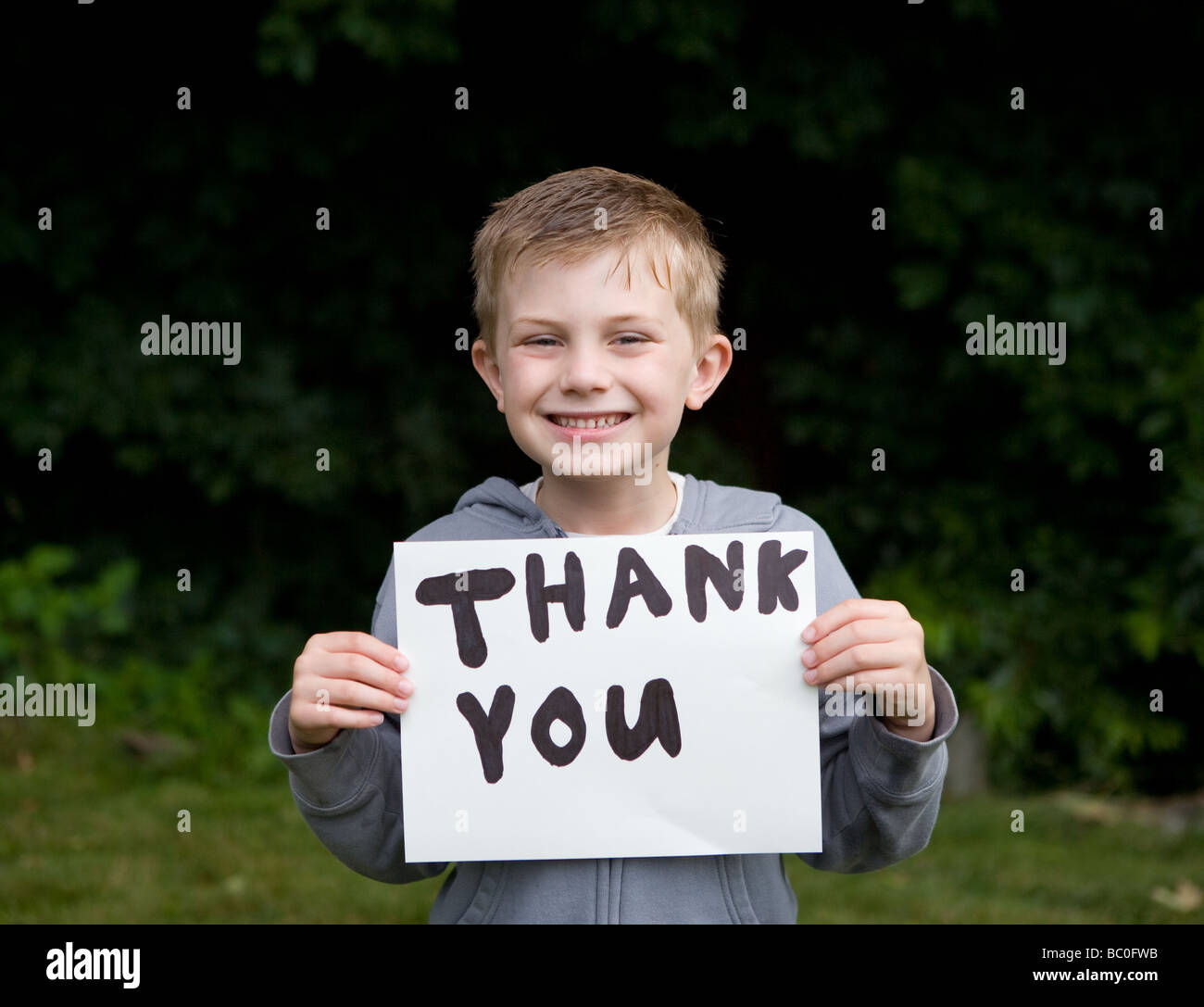 Kleiner Junge lächelnd mit danke auf ein Papier geschrieben Stockfoto
