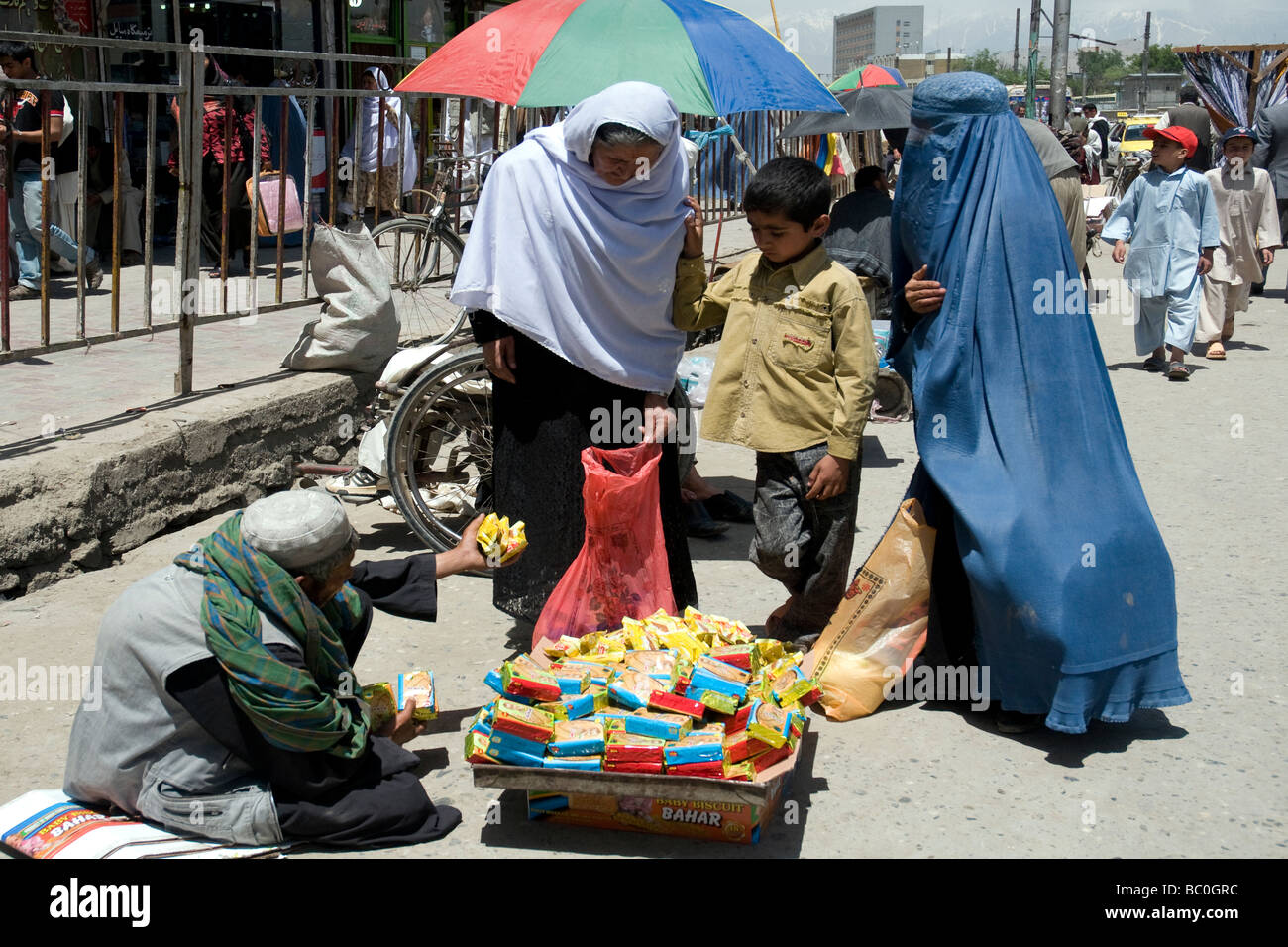 In einem Kabul erwägen City Straße zwei Frauen und ein kleiner Junge kaufen eine Packung Kekse aus einer Straße Hausierer Stockfoto