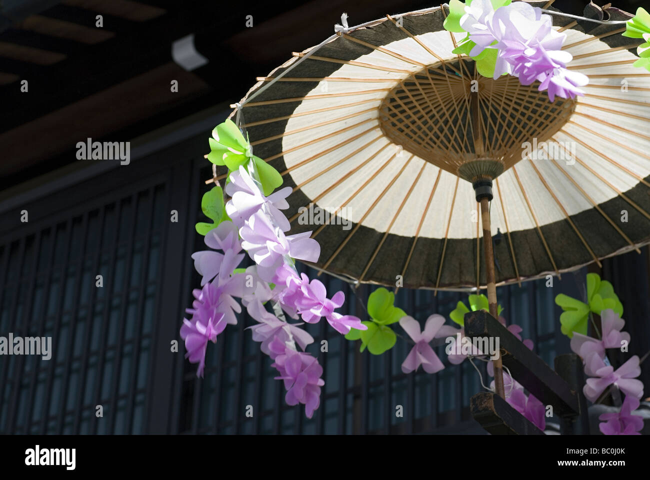 Wind weht Plastikblumen, die einen traditionellen Schirm während des Frühlingsfestes in Takayama schmücken Stockfoto