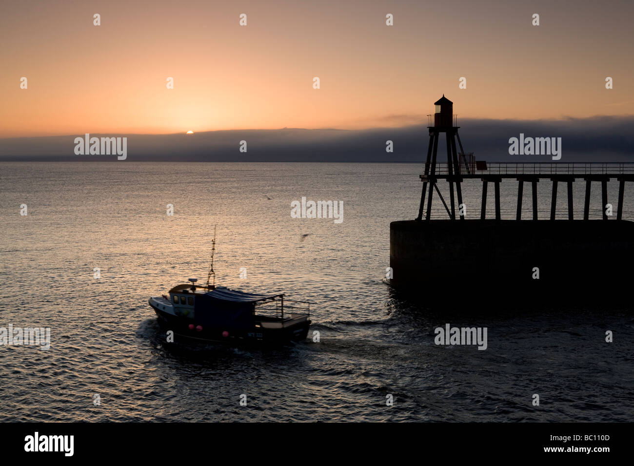 Ein kleines Fischerboot verlässt den Hafen von Whitby, als die Sonne aufgeht Stockfoto