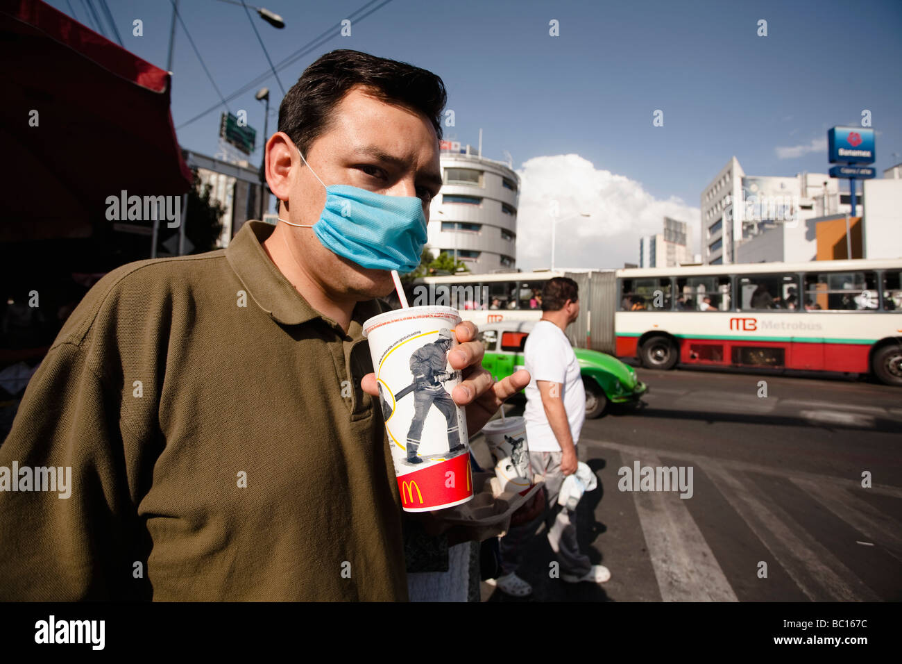 Eine Mann auf der Straße trinkt aus einem McDonalds Cup durch eine blaue Maske während der Schweinegrippe-Epidemie. Stockfoto